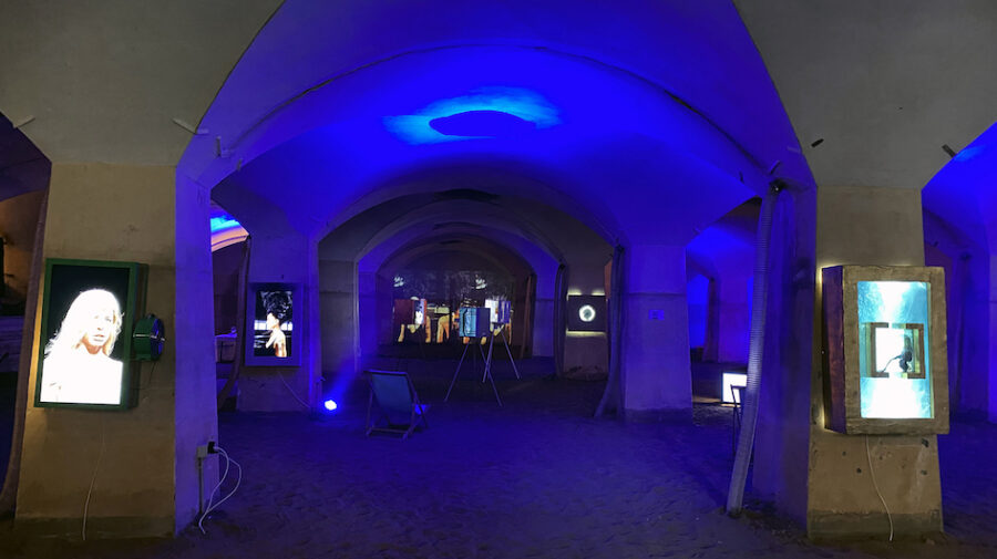 In einem dunkelblau ausgeleuchteten Raum sind mehrere Videoinstallationen angebracht.