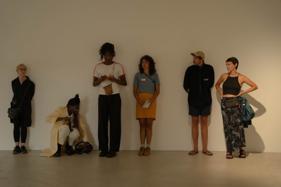 Auf dem Foto sind frontal sechs Personen zu sehen, die vor einer weissen Wand stehen oder knien.